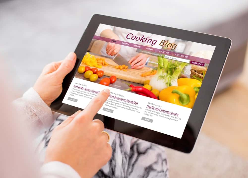 Hands holding a tablet displaying a cooking blog onscreen.